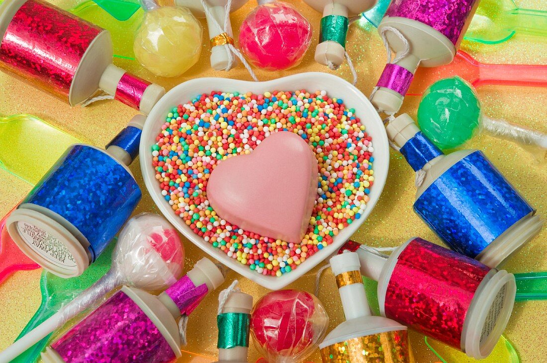 Herzschale mit einem rosa Schokoladenherz, bunte Party Poppers, Lollis und Kunststoffeislöffel