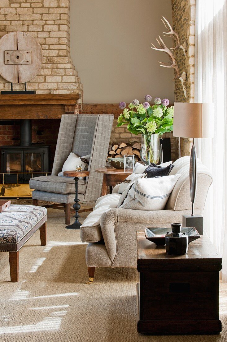 Wood-burning stove in open fireplace with brick chimney breast behind checked grey reading chair; magnificent summer bouquet in corner