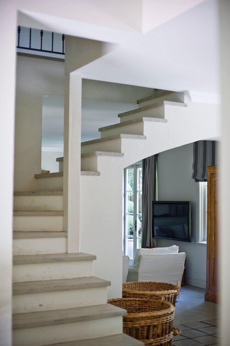 Blick vom Vorraum auf Wendeltreppe in offenem Treppenhaus und weisser Sessel im Durchgang