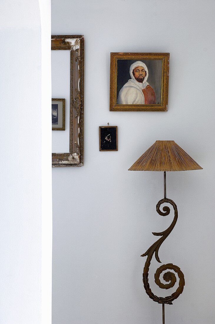 Standleuchte mit gebogenem Metallornament und Lampenschirm vor Wand mit gerahmten Bildern