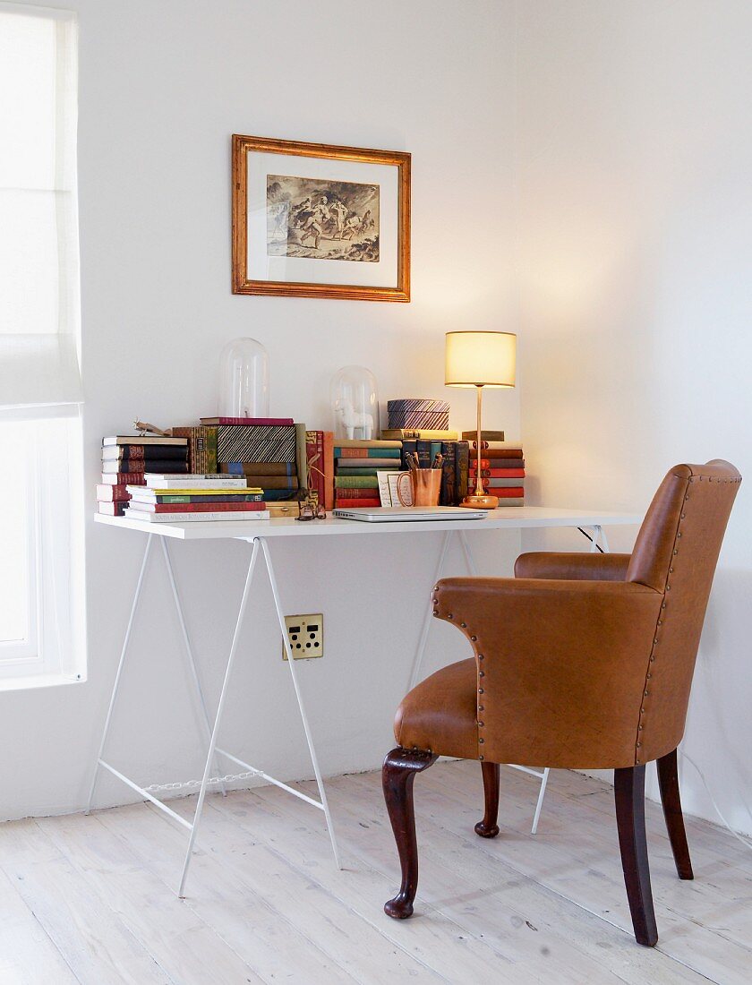Aufgebockter, einfacher Schreibtisch mit antikem Leder-Armstuhl in weisser Zimmerecke