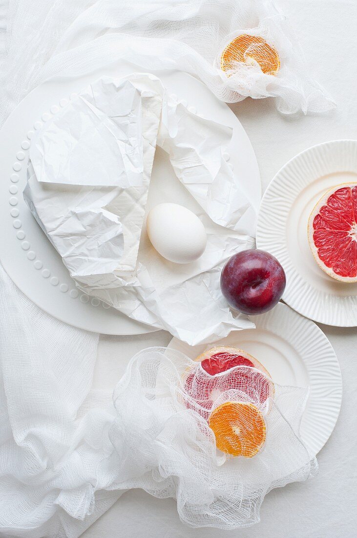 Grapefruit, a plum and an egg on white plates with a muslin cloth