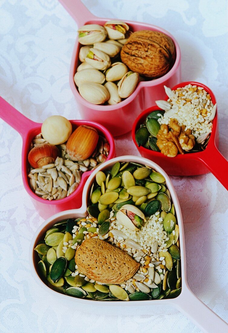 Herzförmige Messbecher mit Kürbiskernen, Sesam, Mandeln, Sonnenblumenkernen, Haselnüssen, Pistazien und Walnüssen