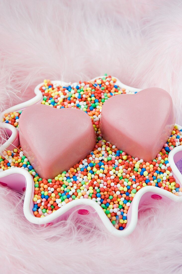 Zwei rosa Schokoladenpralinen auf bunten Zuckerperlen in einer Schale
