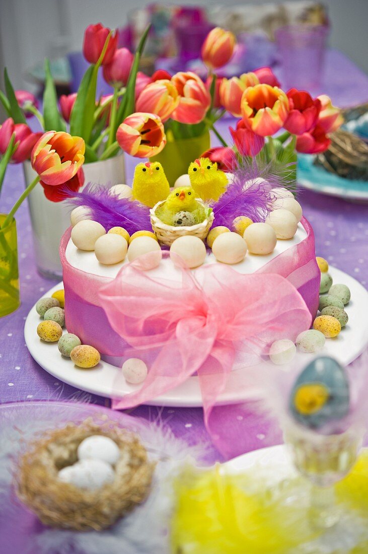 Simnel Cake mit rosa Chiffonband und gelben Osterküken, Tulpen