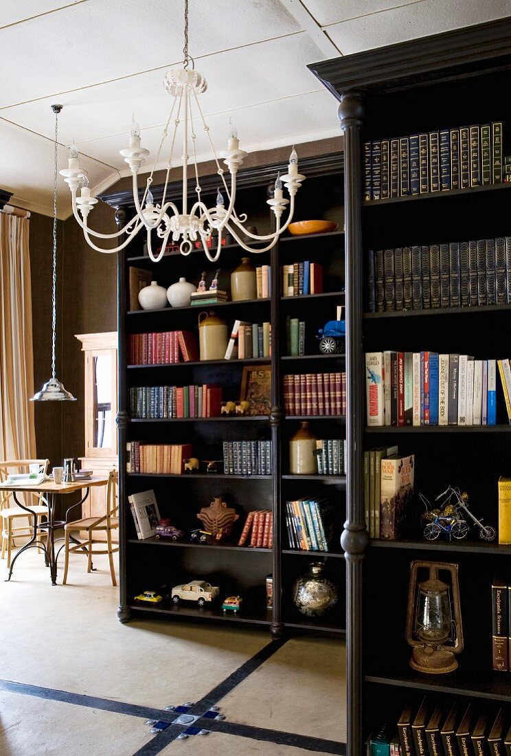 Dark, varnished, free-standing bookcases and white, metal chandelier on ceiling of open-plan living area