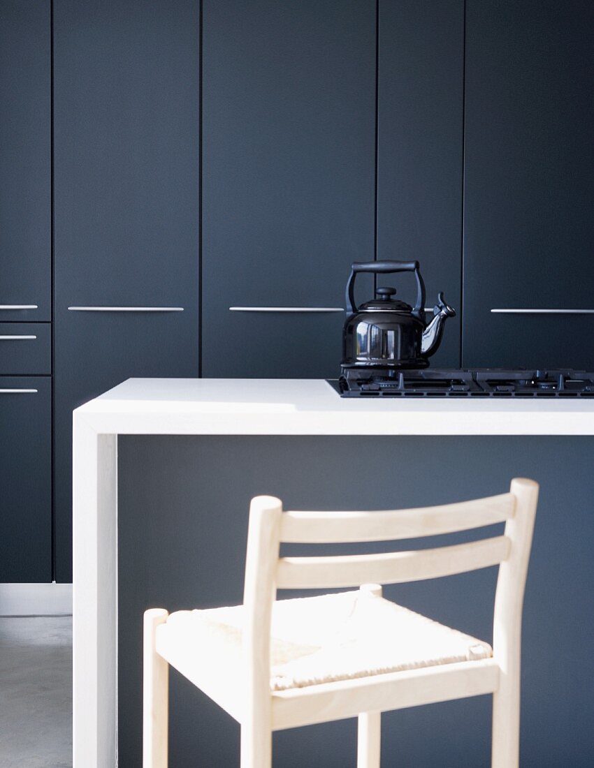 Slate grey fitted cupboard doors behind white island counter; vintage kettle on gas hob