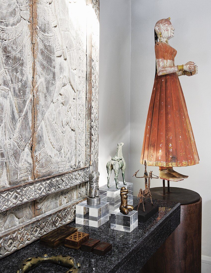 Chinese puppet of woman on pedestal and collection of statues on plexiglass plinths in front of stone relief on stone surface