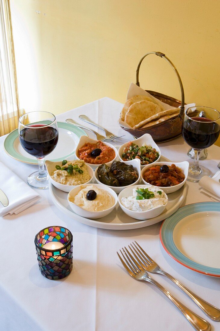 Viele verschiedene mediterrane Dips und Aufstriche auf einem Tisch mit Wein und Fladenbrot