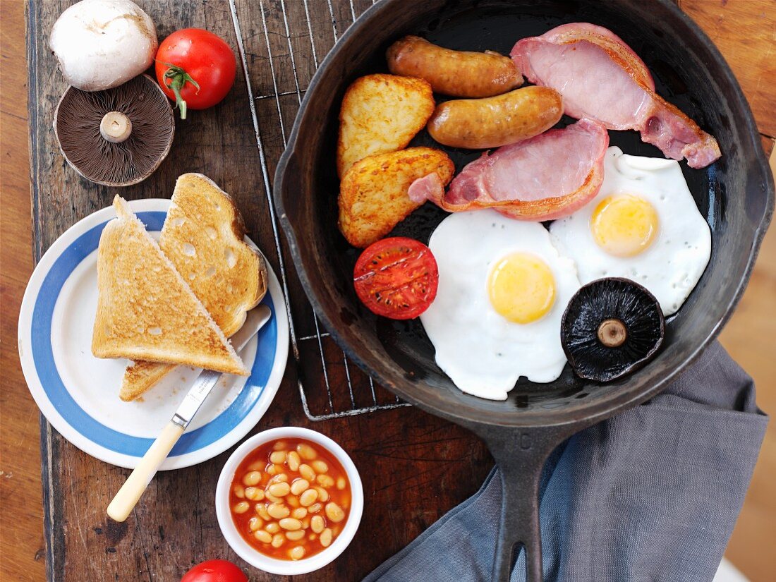 English breakfast with fried eggs, bacon, small sausages, baked beans and toast