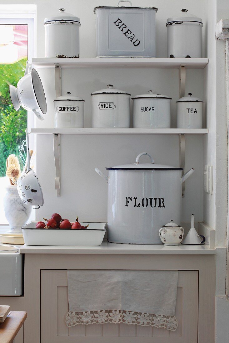 White, vintage enamel tins with lids on bracket shelves next to kitchen window