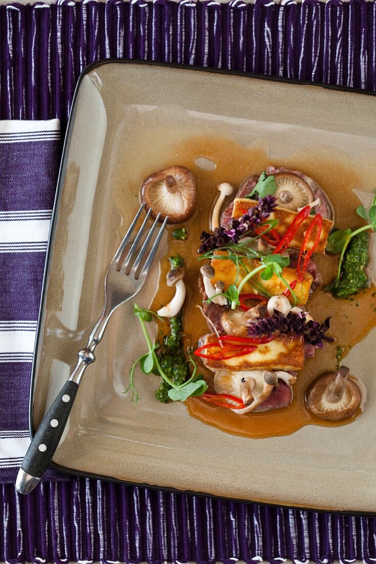 Gebratener Halloumikäse auf Wurstscheiben mit Pilzsauce, Paprika, Kräutersauce und Lavendelblüten