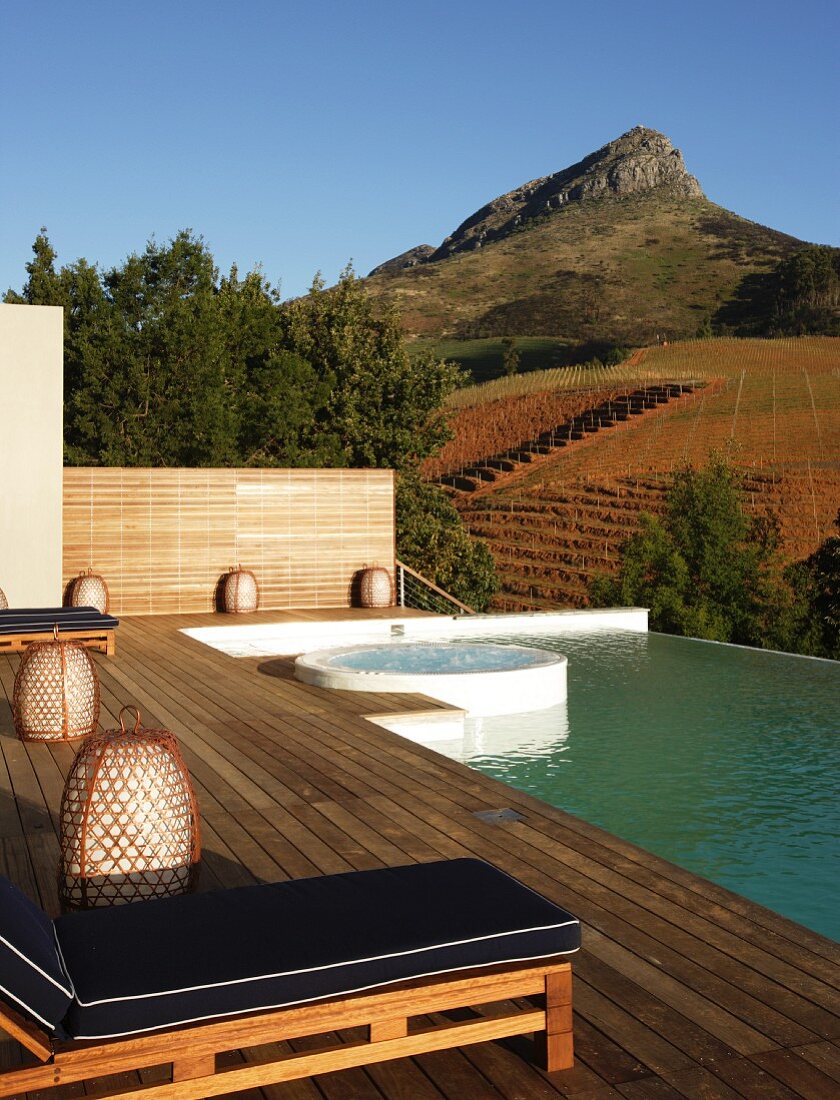 Infinity pool with integrated whirlpool; expansive wooden deck with comfortable sun loungers in foreground