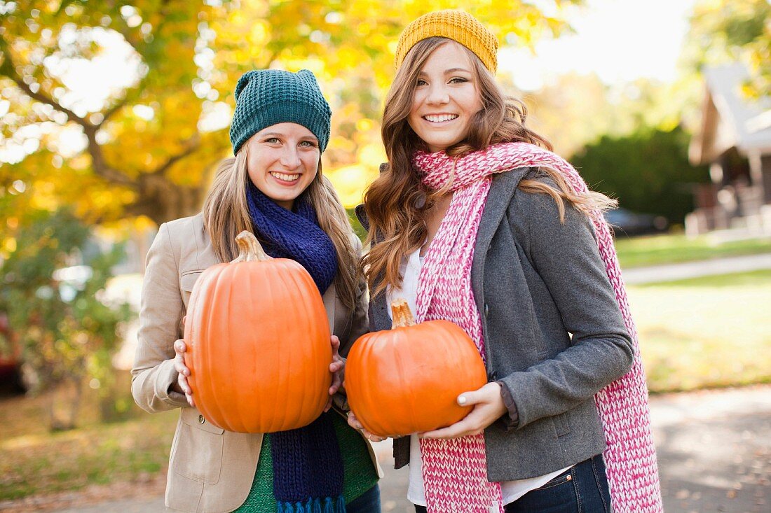 Two women holding orange pumpkins