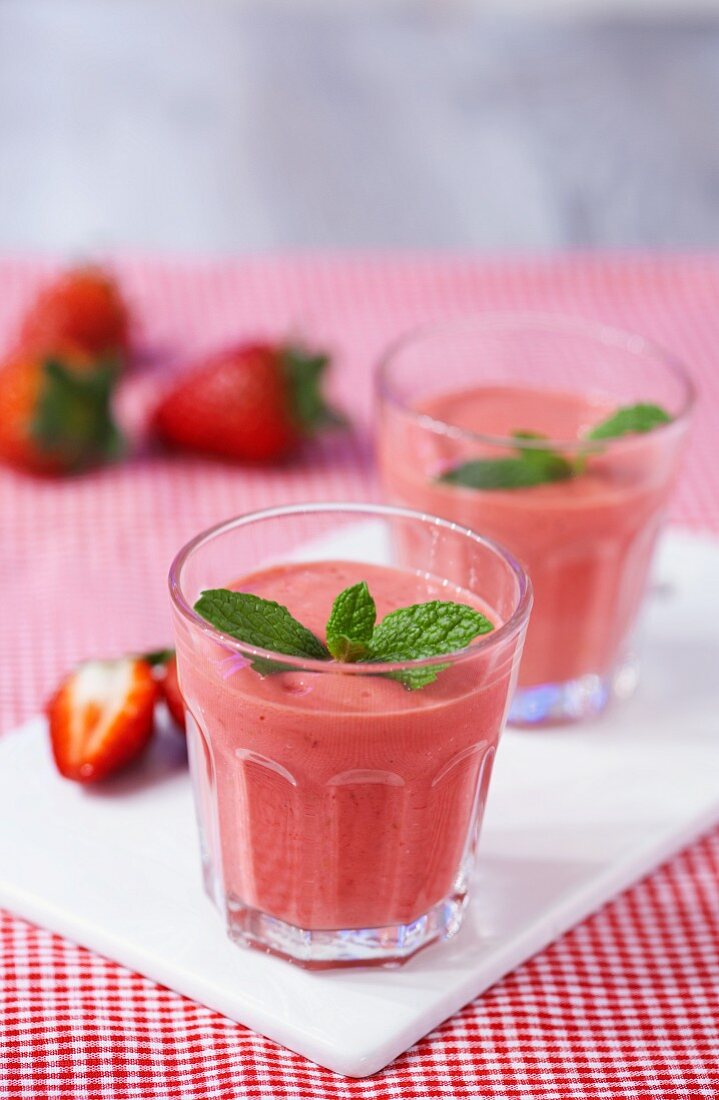 Strawberry smoothies topped with mint leaves on a chopping board on a red gingham tablecloth