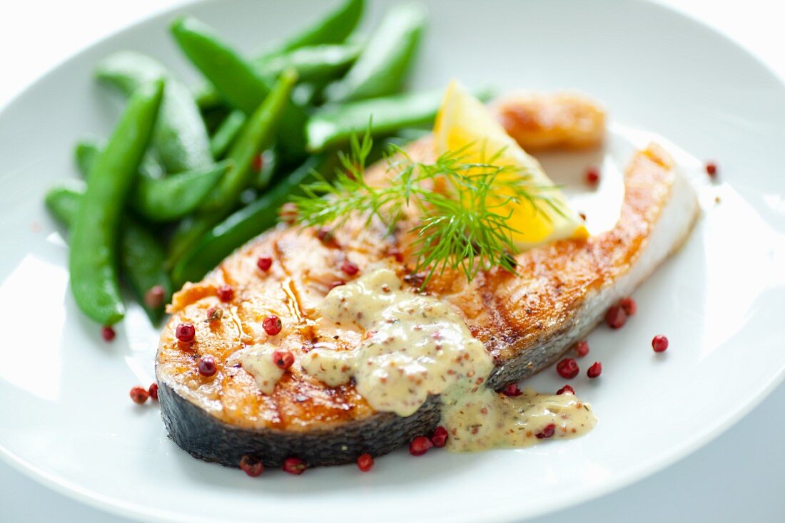 Fried salmon steak with sugar snap peas, honey and mustard sauce and red peppercorns