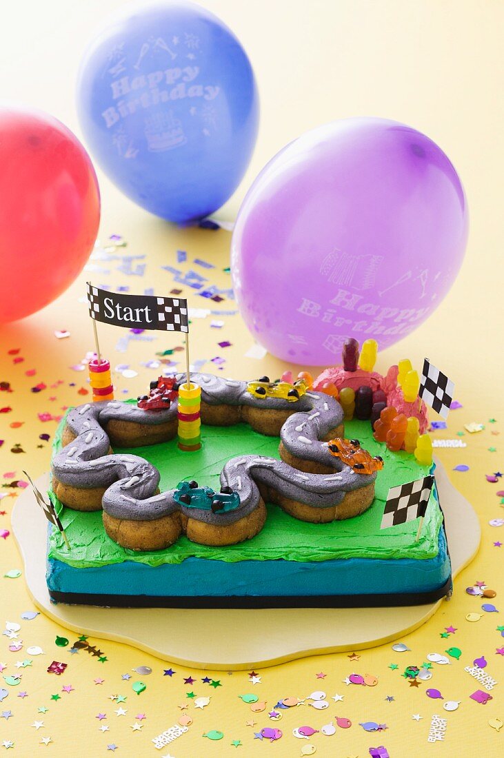 A child's birthday cake (a racing track) and balloons