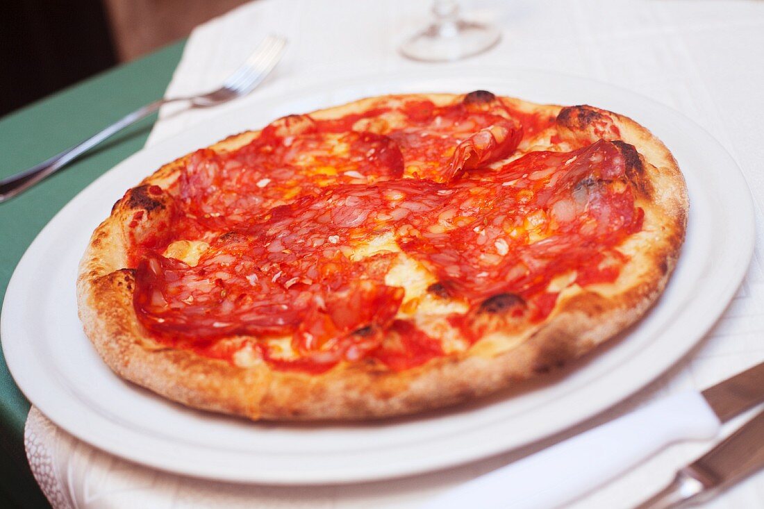 Whole Prosciutto Pizza on a White Plate on a Restaurant Table