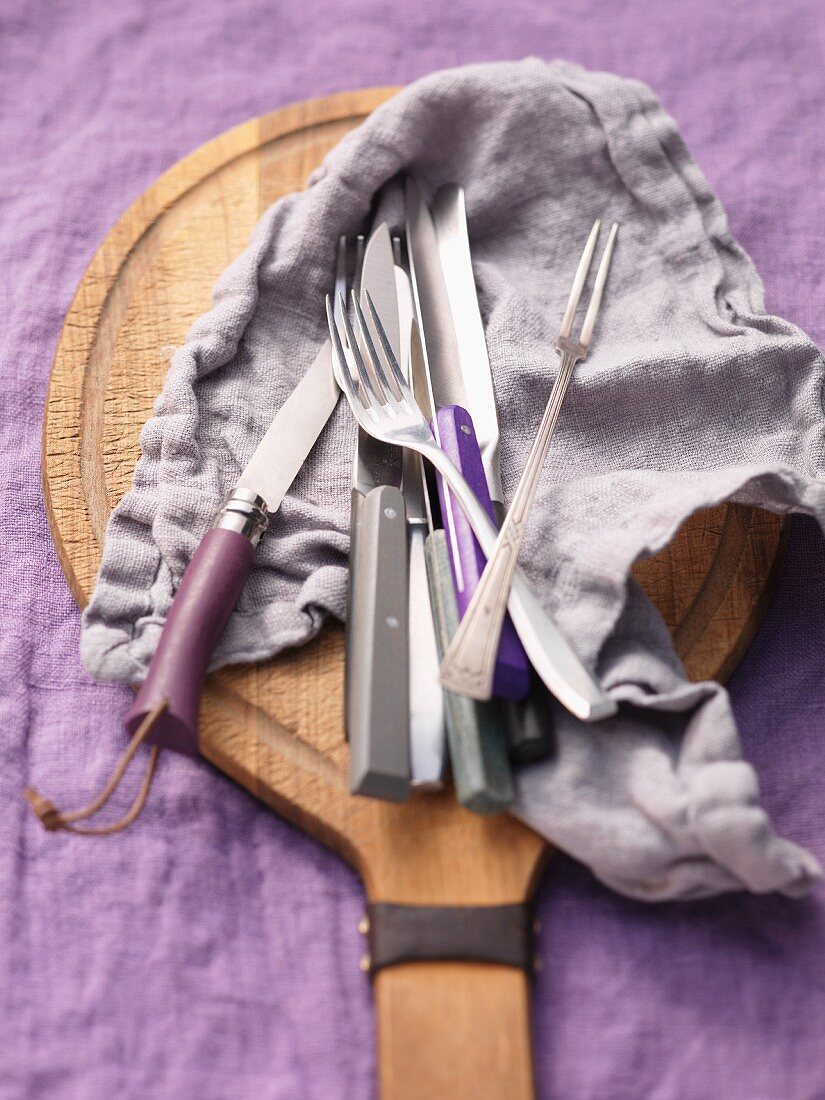 Knives, a fork and a serving fork lying on a cloth on a wooden board