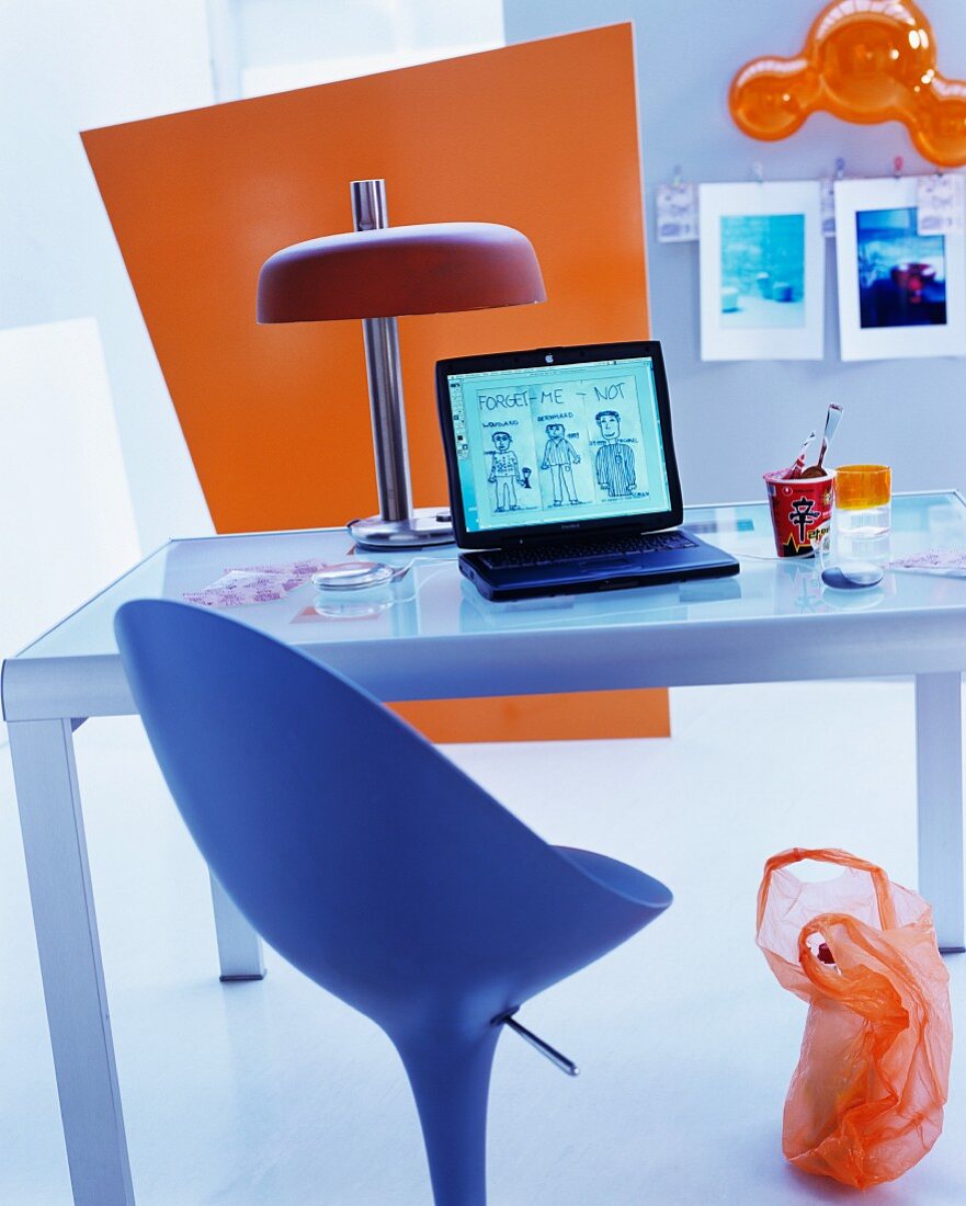 Designer Drehstuhl vor Glasschreibtisch mit Retro-Tischlampe und farbiges Paneel