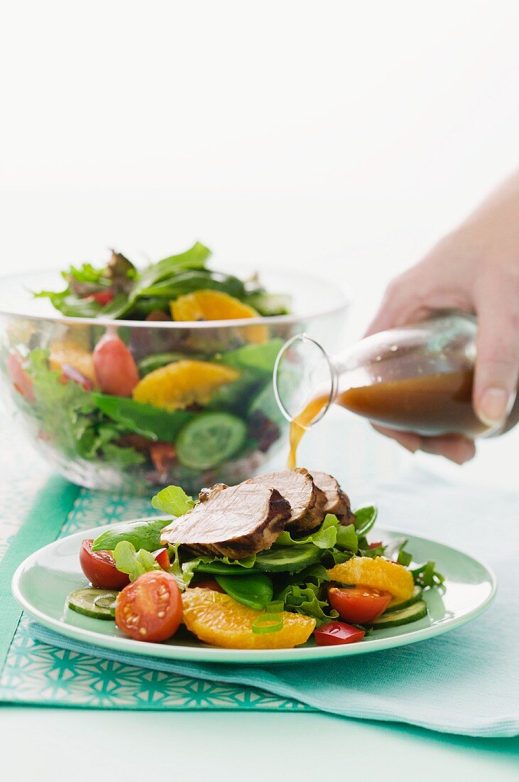 Dressing being poured over roast pork on orange salad