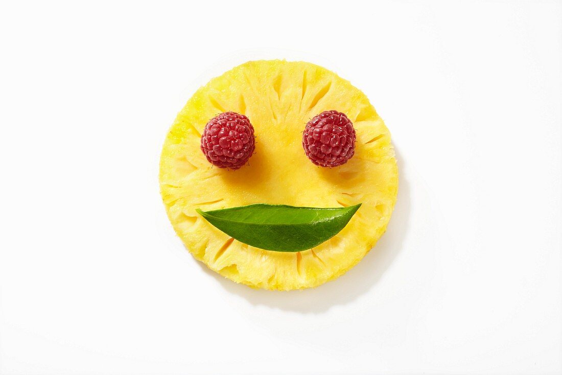 Lächelndes Obstgesicht aus Ananas, Himbeeren und Blatt