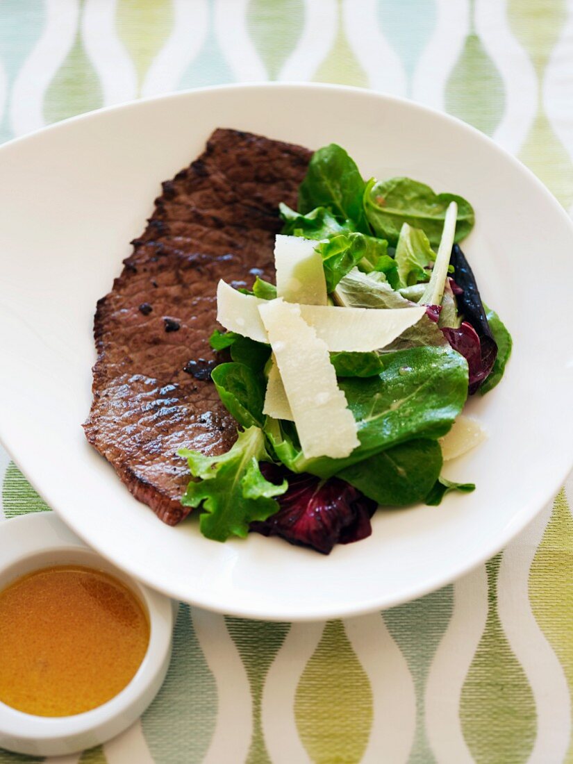 Steak Served with Salad with Shaved Parmesan Cheese; On a White Plate