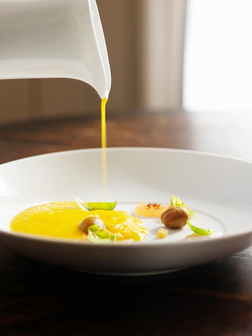 Pouring Smooth and Creamy Squash Soup into a White Bowl with Garnishes