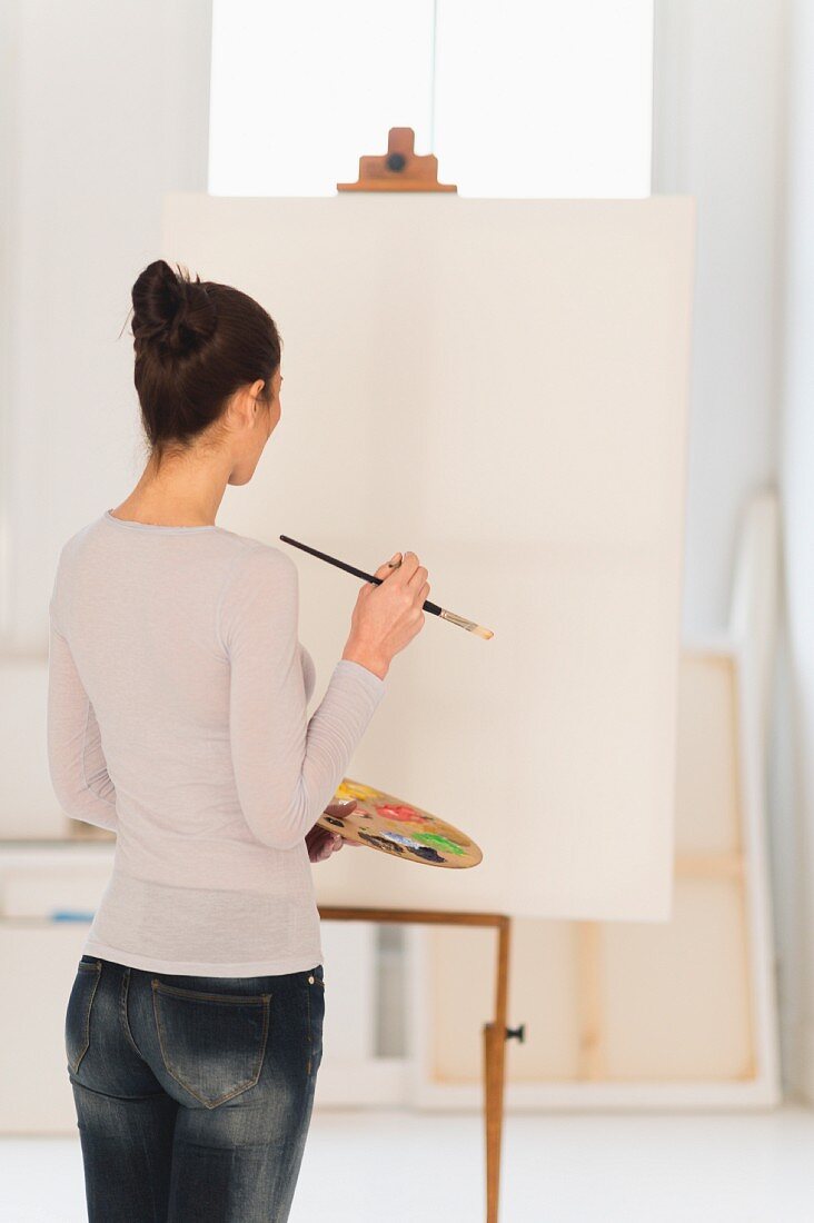 Woman standing in front of blank canvas on easel in artist's studio