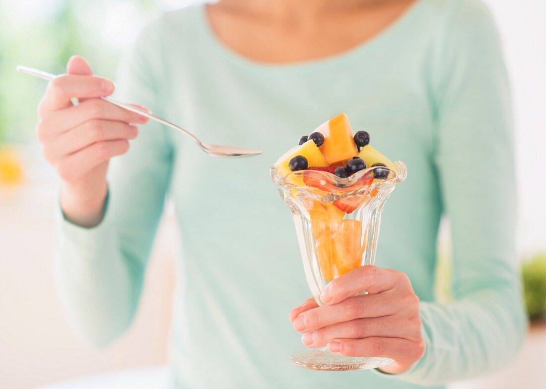 A woman holding a sundae glass of fruit salad