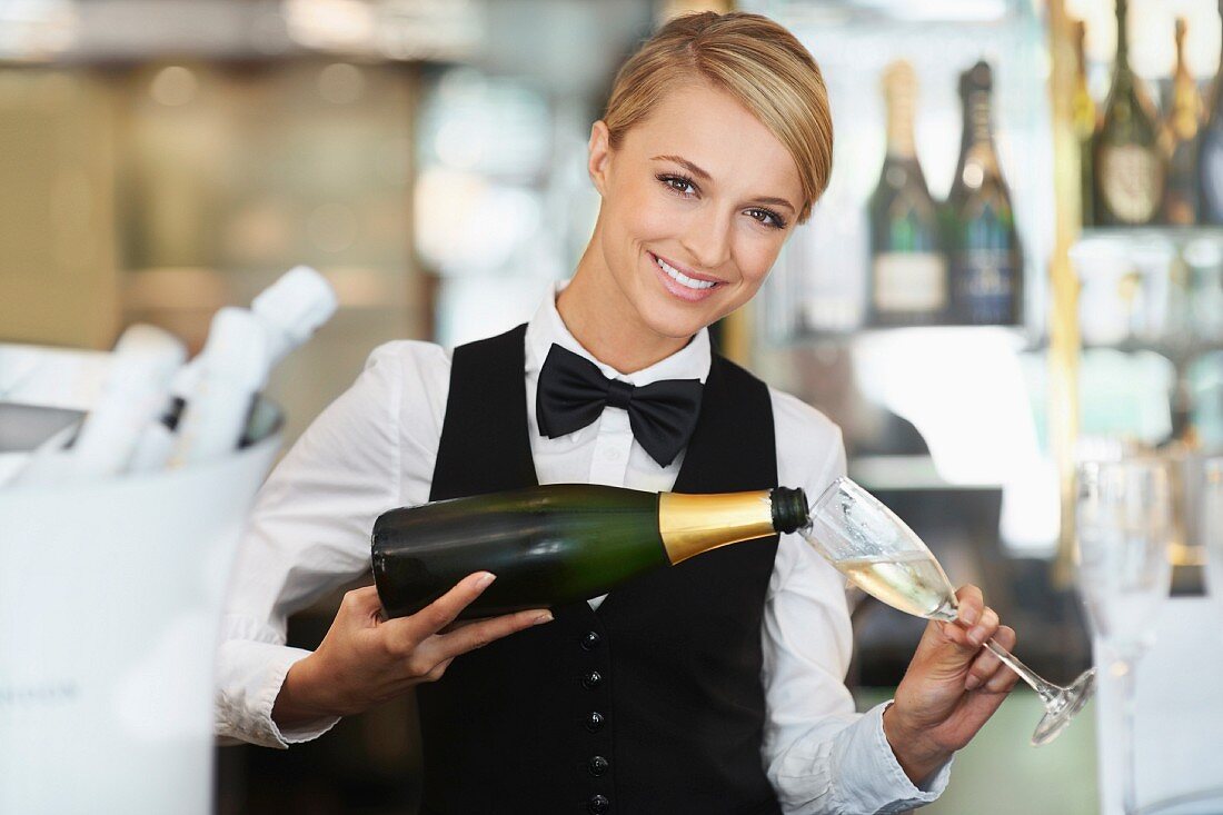 A waitress pouring sparkling wine in a restaurant