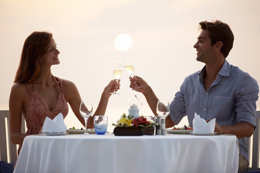 A couple clinking glasses of sparkling wine with a romantic dinner by the sea