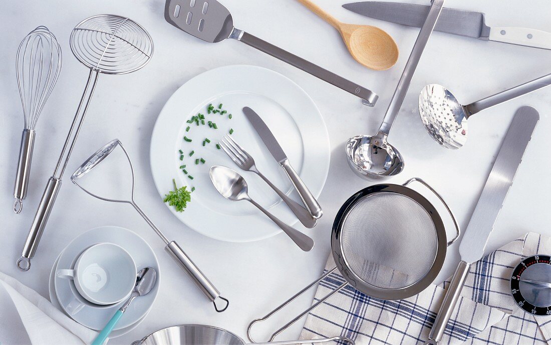Assorted kitchen utensils, cutlery, a plate, a cup, a kitchen timer and a tea towel