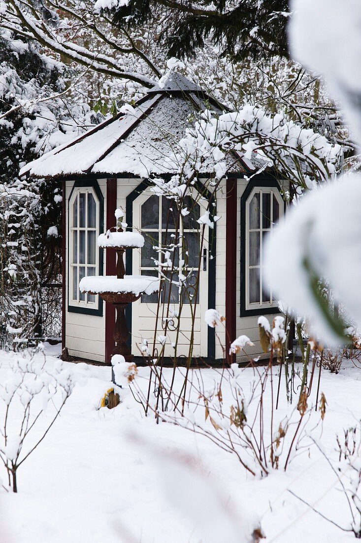 Summerhouse and birdbath in snowy garden