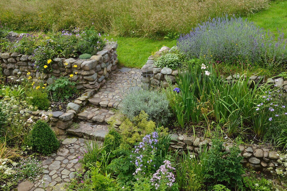 Blühender Cottagegarten mit Natursteinmauern und Gartenweg mit Natursteinpflaster