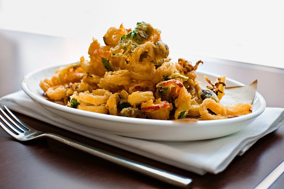 Fried Calamari Plated on an Oval White Plate; On a Folded White Napkin with a Fork