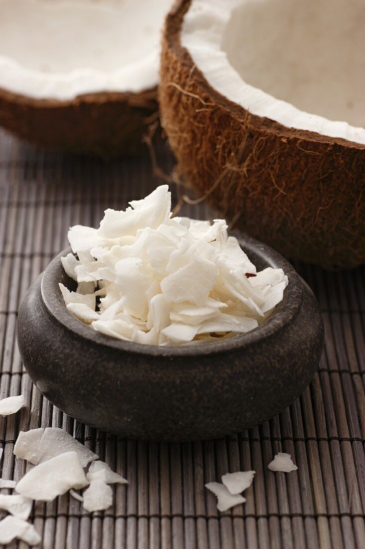 A coconut, broken open, and coconut shavings, on a bamboo mat (close-up)