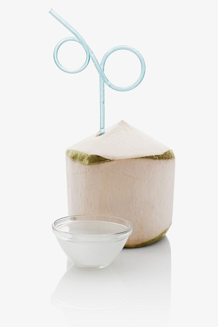 A peeled coconut with a drinking straw and a small bowl of coconut water