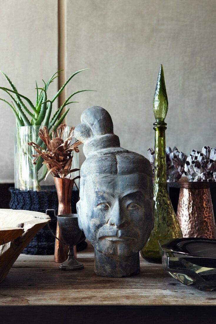 Asiatischer Kopf aus Stein und Vasen aus verschiedenen Materialien auf Holztisch