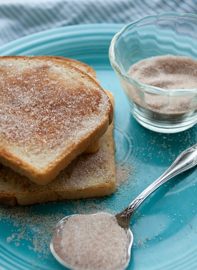 Toast mit Zimtzucker auf einem blauen Teller, Glas und Löffel mit Zimt-Zucker-Mischung