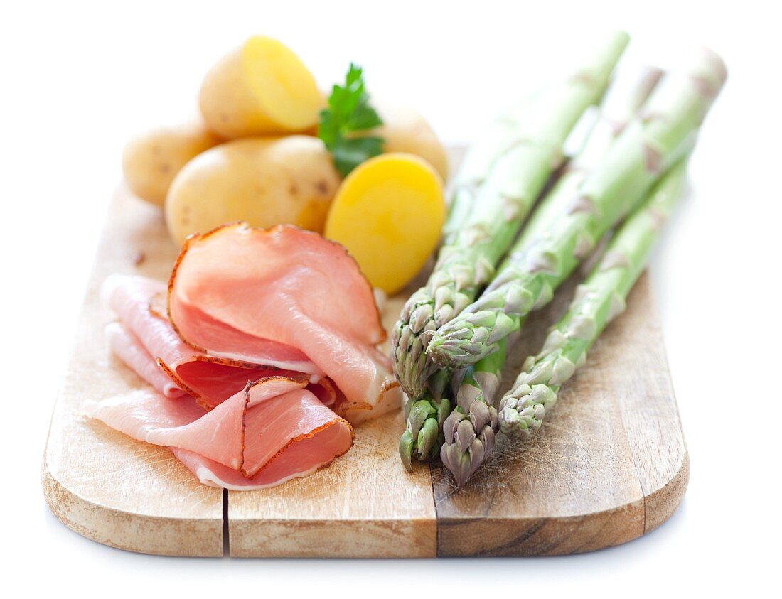 Green asparagus, ham and potatoes on a chopping board