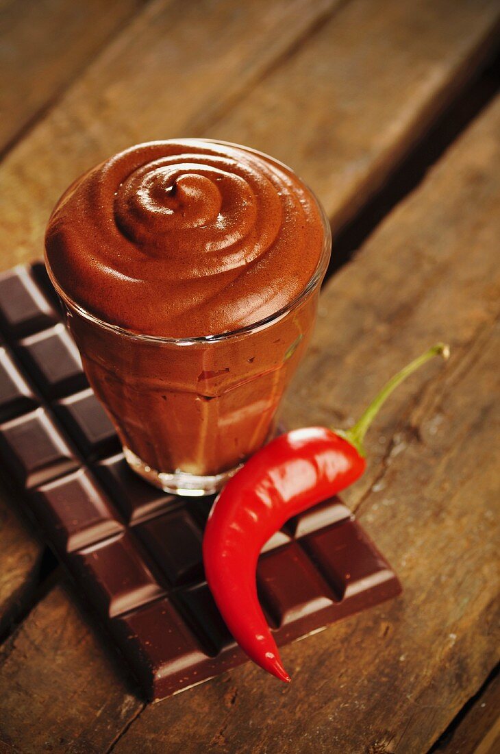 Ein Glas Schokoladenmousse und Chilischote auf einer Schokoladentafel