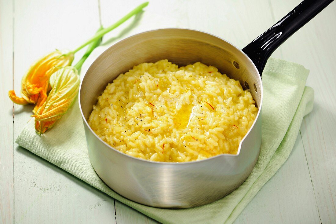 Saffron risotto in a pan, zucchini blossoms in the background