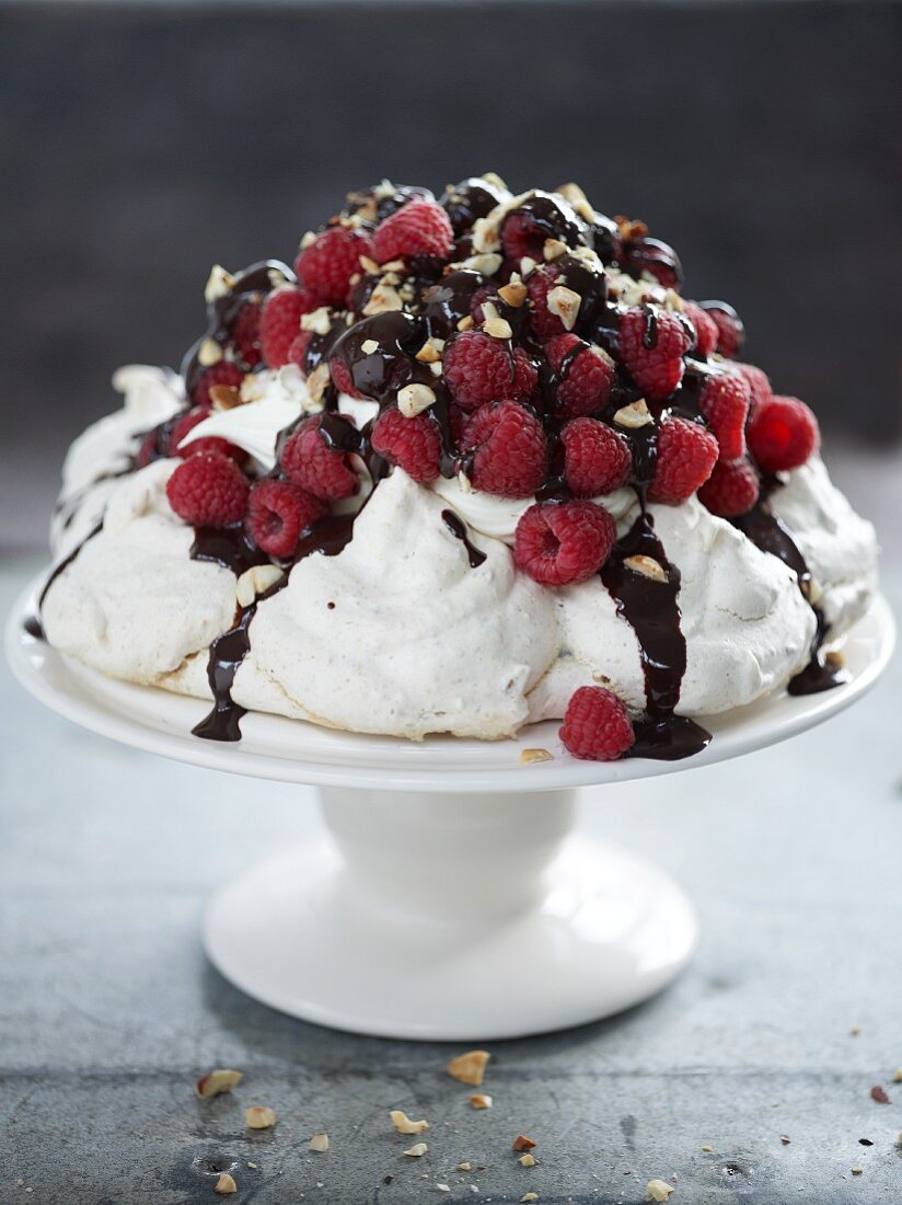 A pavlova with raspberries, chocolate sauce and nuts