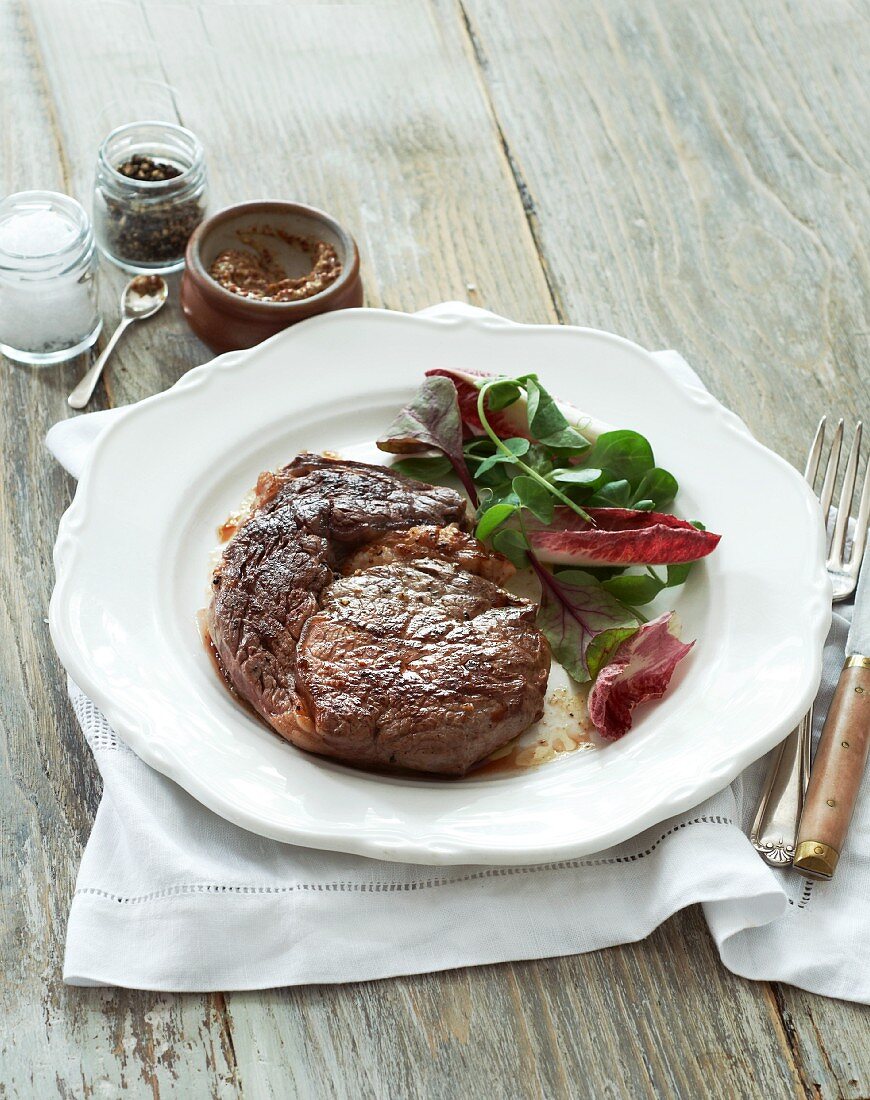 Beef steak with salad leaves, mustard, salt and pepper