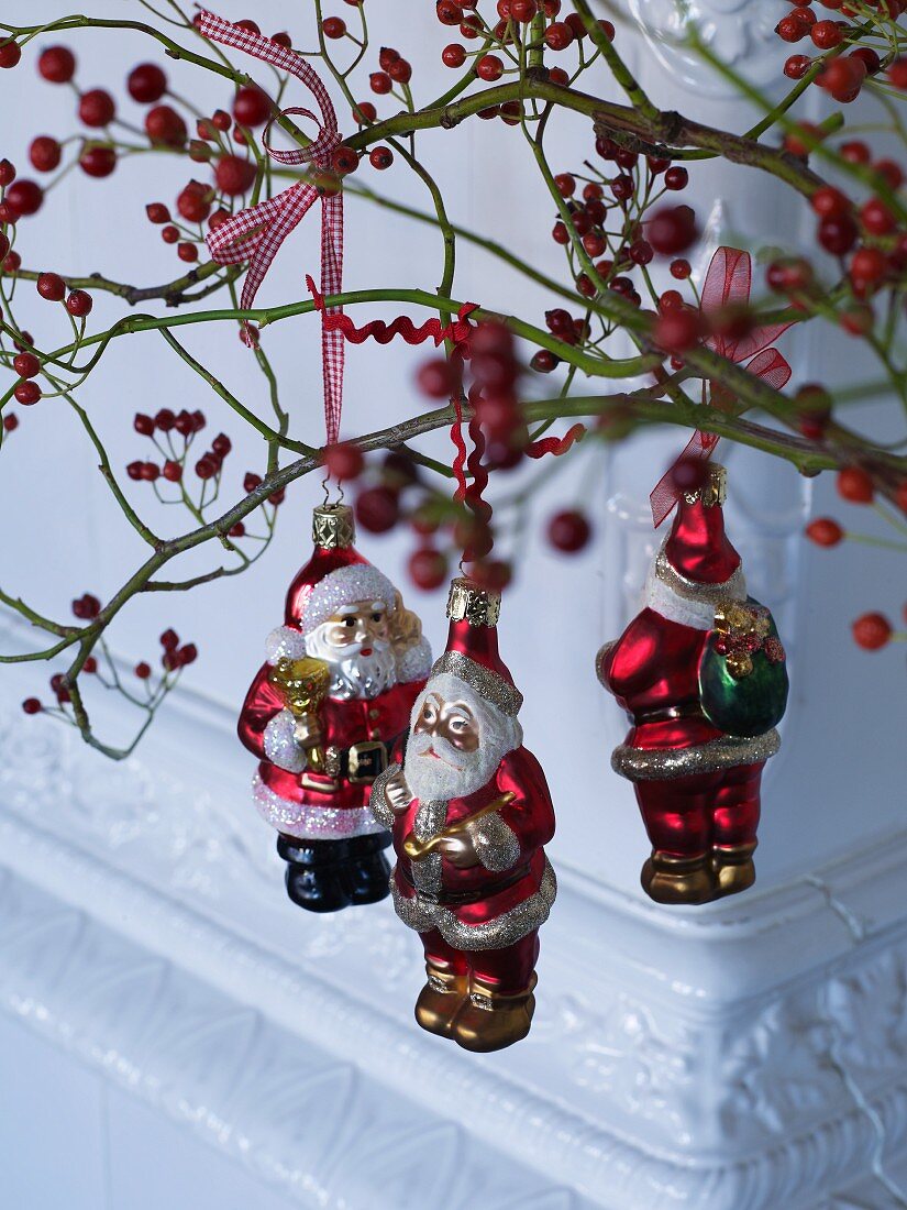 Weihnachtsmänner als Baumfiguren an roten Beerenzweigen aufgehängt