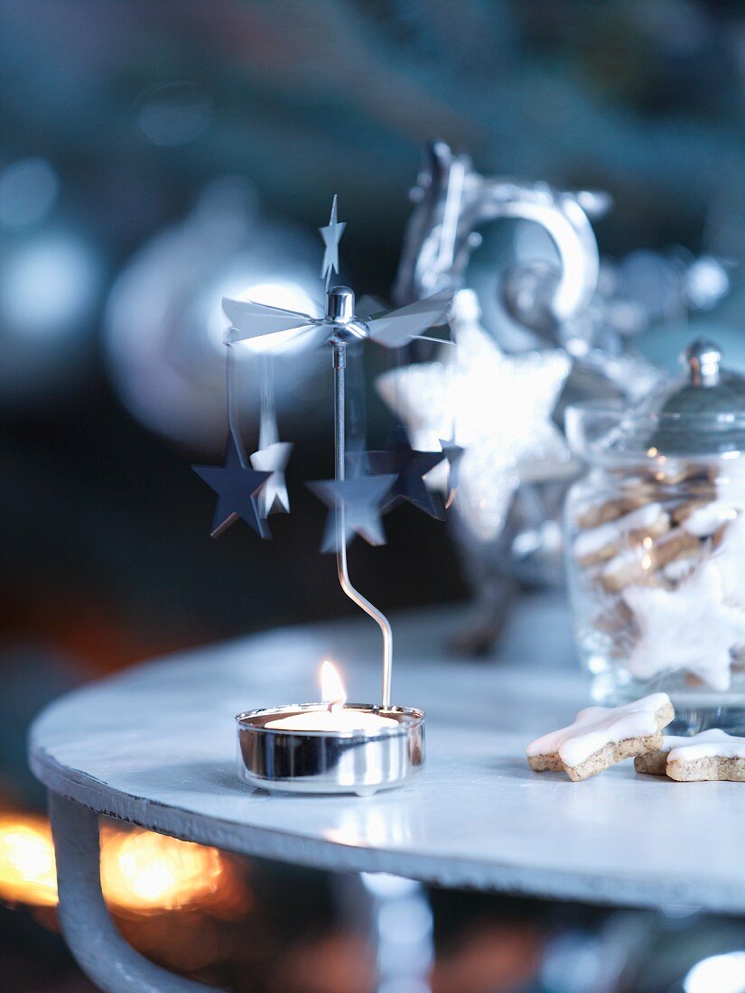 Tealight carousel with lit candle next to storage jar of festive biscuits on side table