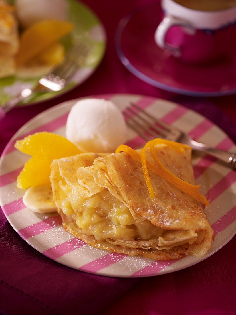 A pancake with stewed banana, orange pieces and vanilla ice cream