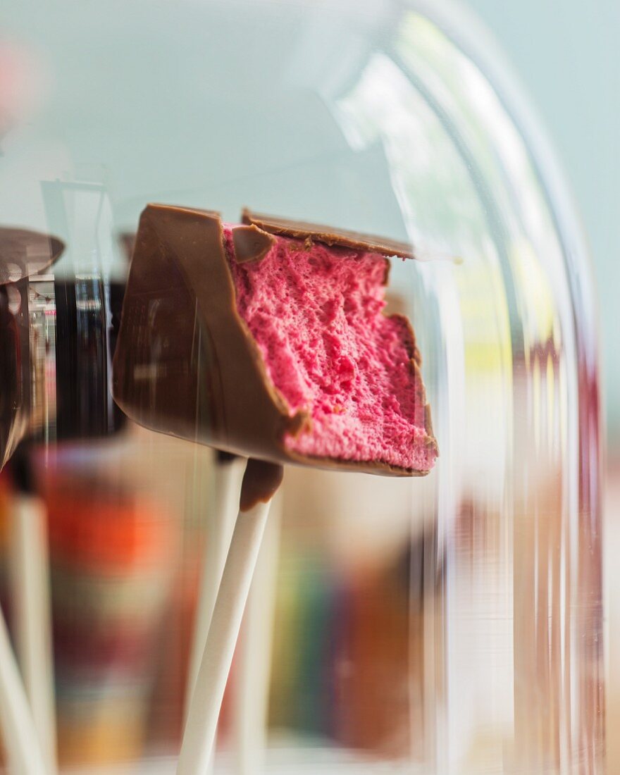 A marshmallow with chocolate coating on a stick (a bite missing)