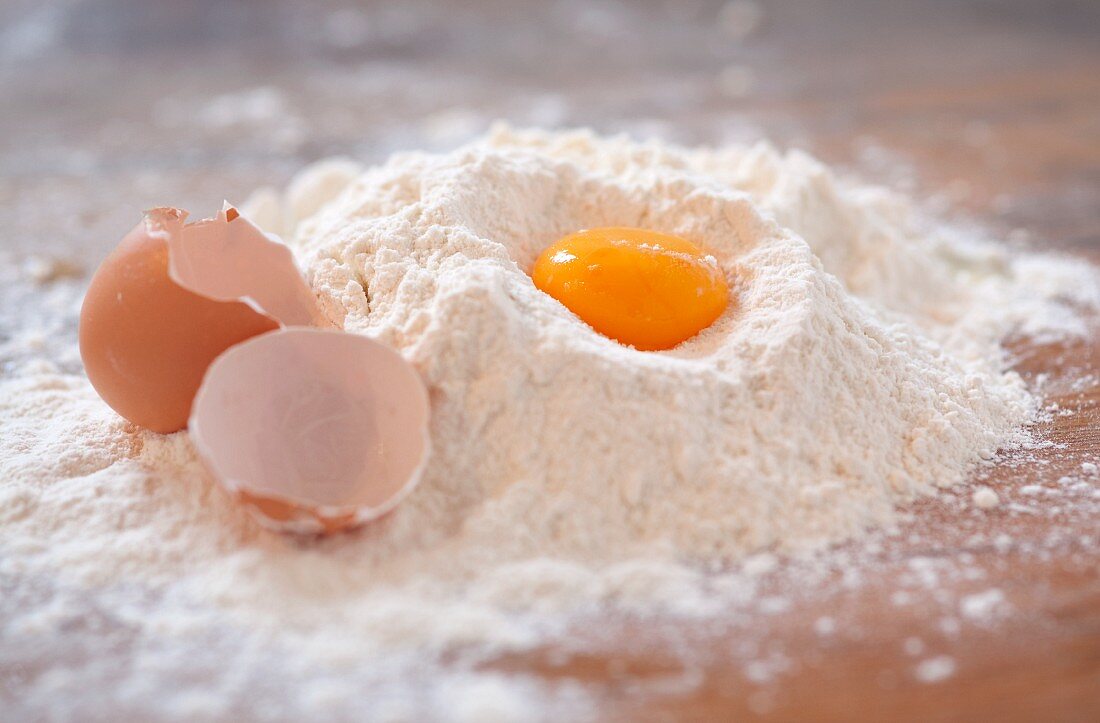 An egg yolk and an eggshell in flour on a wooden slab